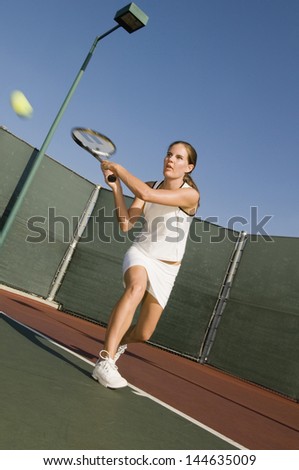 Full length of a female tennis player hitting backhand on the tennis court