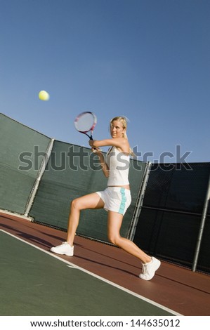 Full length of a female tennis player hitting backhand on the tennis court