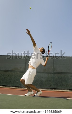Side view of a male tennis player serving ball on court
