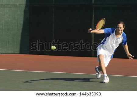 Full length of a male tennis player hitting backhand on the tennis court