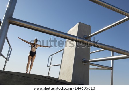 Rear view of a female diver with arms out about to dive against the blue sky