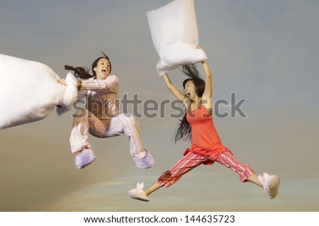 Two multiethnic young women having pillow fight midair outdoors