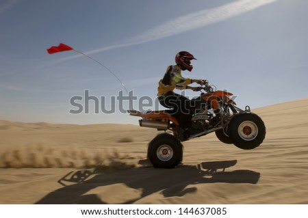 Side view of a quad bike rider doing wheelie in desert against the sky