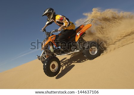 Low Angle View Of A Man Riding Quad Bike In Desert Against The Blue Sky
