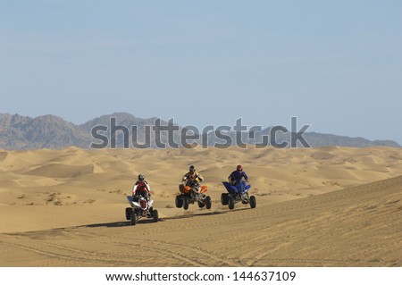 Three men riding quad bikes in a row at the desert