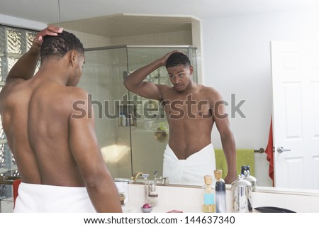 Young African American man looking at self in bathroom mirror