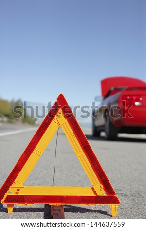 Warning triangle in front of broken down red sports car at side of road
