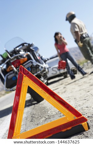 Closeup of a warning triangle sign with police and woman on call by motorcycle and stopped car