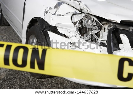 Closeup of a cropped damaged car behind warning tape at an accident scene