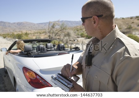 Closeup of a police officer writing traffic ticket to woman sitting in car