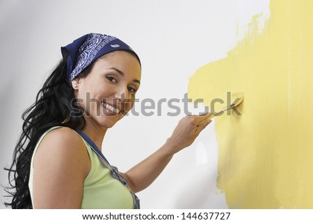 Side view of a happy young woman painting the wall yellow
