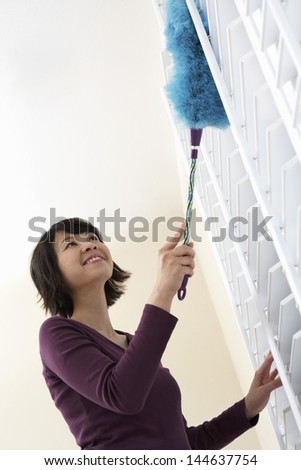 Low angle view of a smiling Asian woman dusting window