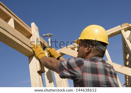Low angle view of a construction worker hammering nail on timber frame against clear blue sky