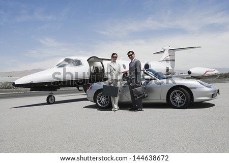 Portrait of a business couple standing in front of convertible and private jet on landing strip
