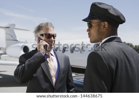 Chauffeur looking at senior businessman on call with private jet in the background