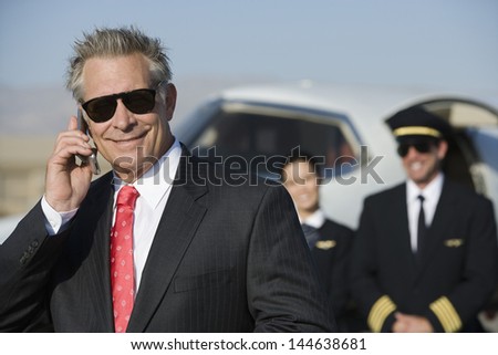 Portrait of smiling businessman on call with blurred pilot and flight attendant standing in the background