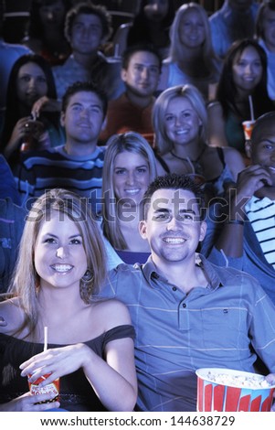 Group of happy multiethnic people with soda and popcorn watching movie in theatre