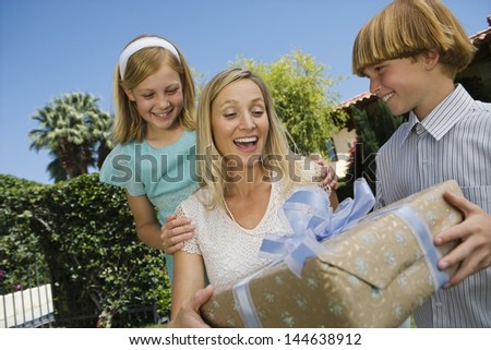 Boy giving birthday present to his surprised mother with a girl outdoors