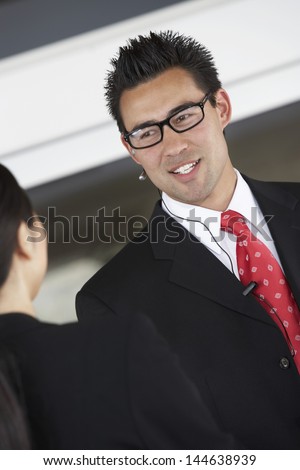 Smiling businessman using hands free device while talking to female colleague