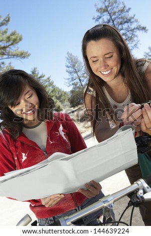 Happy two multiethnic young women with mountain bikes reading a map