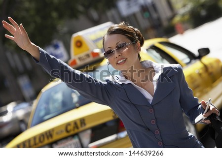 Asian businesswoman hailing cab while using cellphone with hands free device