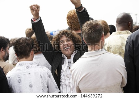 Happy man raising hands with rear view of people together against clear sky