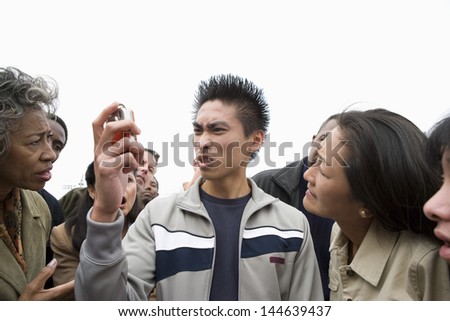 Young man looking at phone in anger with people in the background