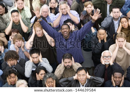 Portrait of a happy African American man raising hands while people covering their ears