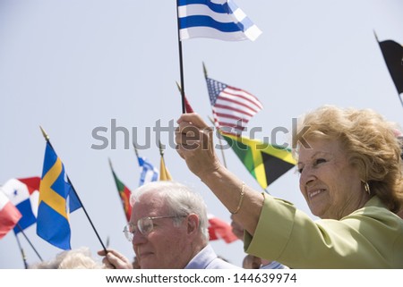 Multiethnic people raising flags of different countries against clear sky
