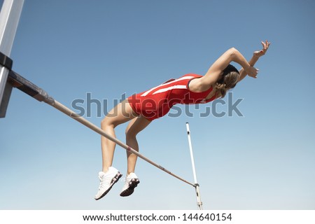 Low angle view of a female high jumper in midair over bar against blue sky