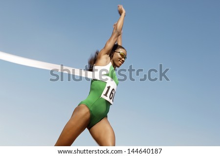 Side view of a female runner winning race against the blue sky