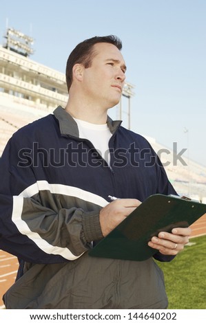 Coach with clipboard standing by running track
