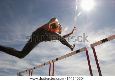 Low Angle View Of A Male Athlete Jumping Hurdle Against The Sky