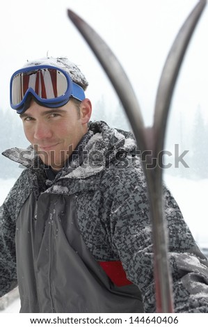 Portrait of a young man wearing ski goggles on head with skis in snow