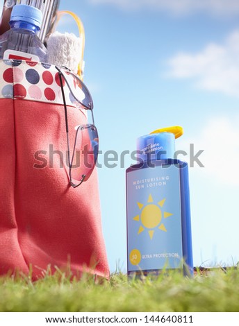 Bottle of suntan lotion and bag with beach items in grass close-up