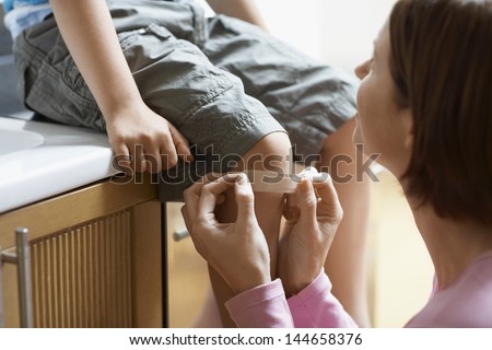 Mother Applying Bandage On Her Son\'S Knee At Home