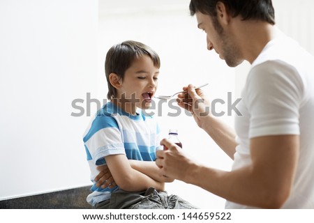 Father giving son cough syrup at home