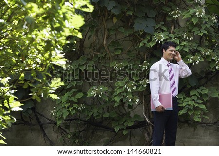 Portrait of smiling young businessman talking on cell phone in park