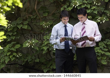 Happy young businessmen reviewing documents in garden