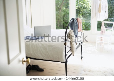 Clothes hanging around bedroom with laptop on bed
