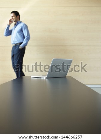 Young businessman using cell phone with laptop on table in foreground