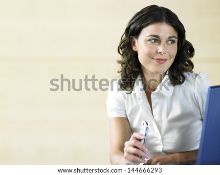 Beautiful young woman holding cell phone while using laptop in office