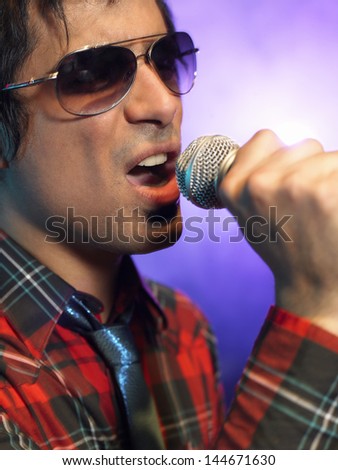 Closeup of a young man singing into microphone on stage at concert