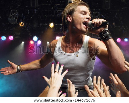 Young man singing on stage in concert with adoring fans reaching towards him