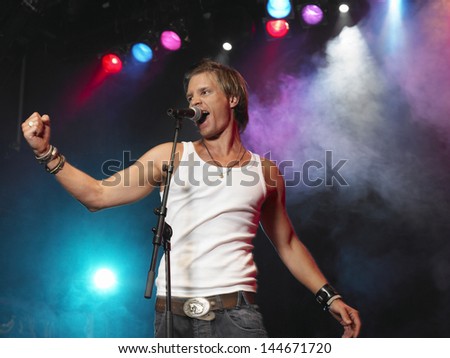 Young man singing into microphone on stage at concert