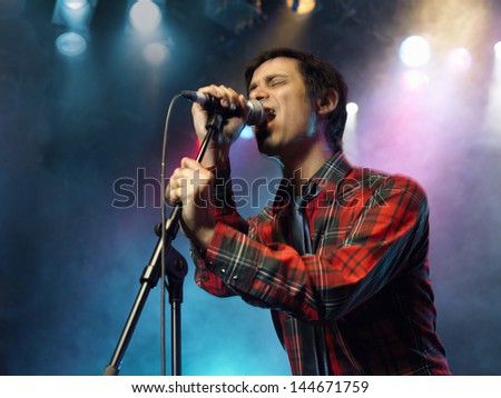 Low angle view of a young man singing into microphone on stage