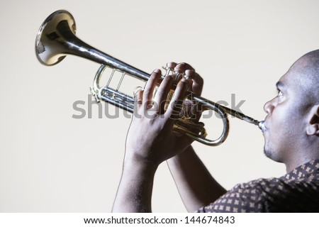 Side view of an African American man playing trumpet against gray background