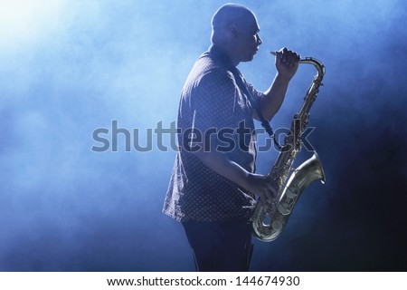 Side View Of An African American Man Playing Saxophone Against Smoky Background