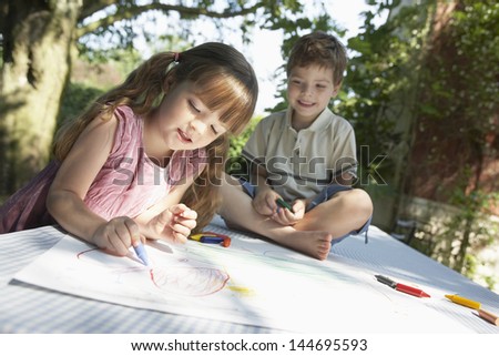 Young boy and girl drawing on table in back garden