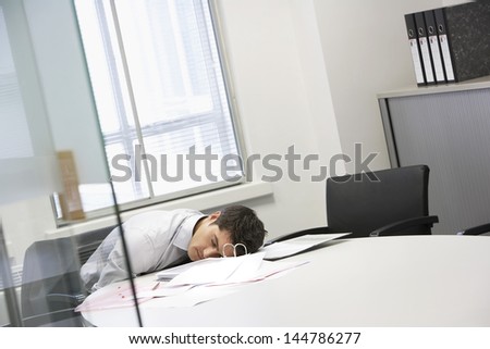 Businessman asleep at desk by scattered files in the office